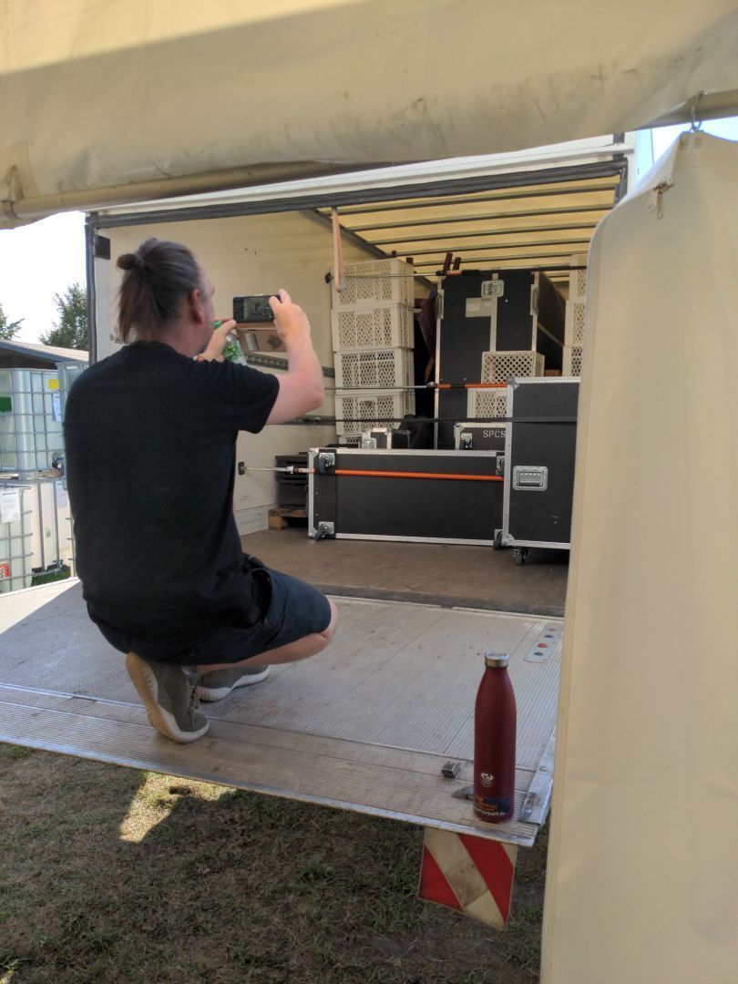 Ein Mensch auf einer Laderampe eines LKW. Der LKW ist reichlich beladen mit flight cases und Boxen.